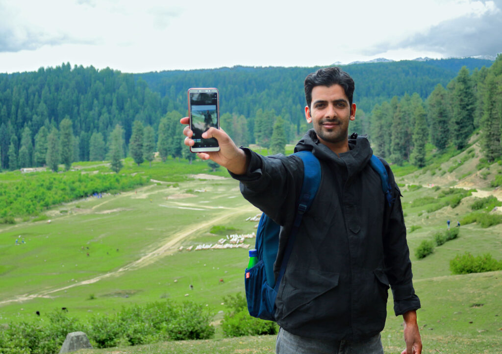 Mountaineer displaying his phone at the top of the mountain.